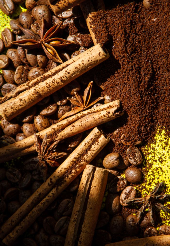 Close-up of cinnamon sticks, coffee beans, star anise, and ground coffee in a vibrant composition.