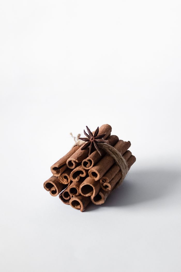 A rustic bundle of cinnamon sticks tied with twine and anise on a white surface, perfect for culinary themes.